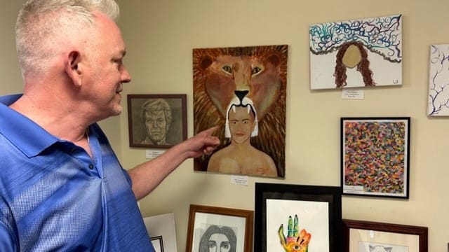 Doug Reinford points at his work on display at the Artists in Recovery exhibit.