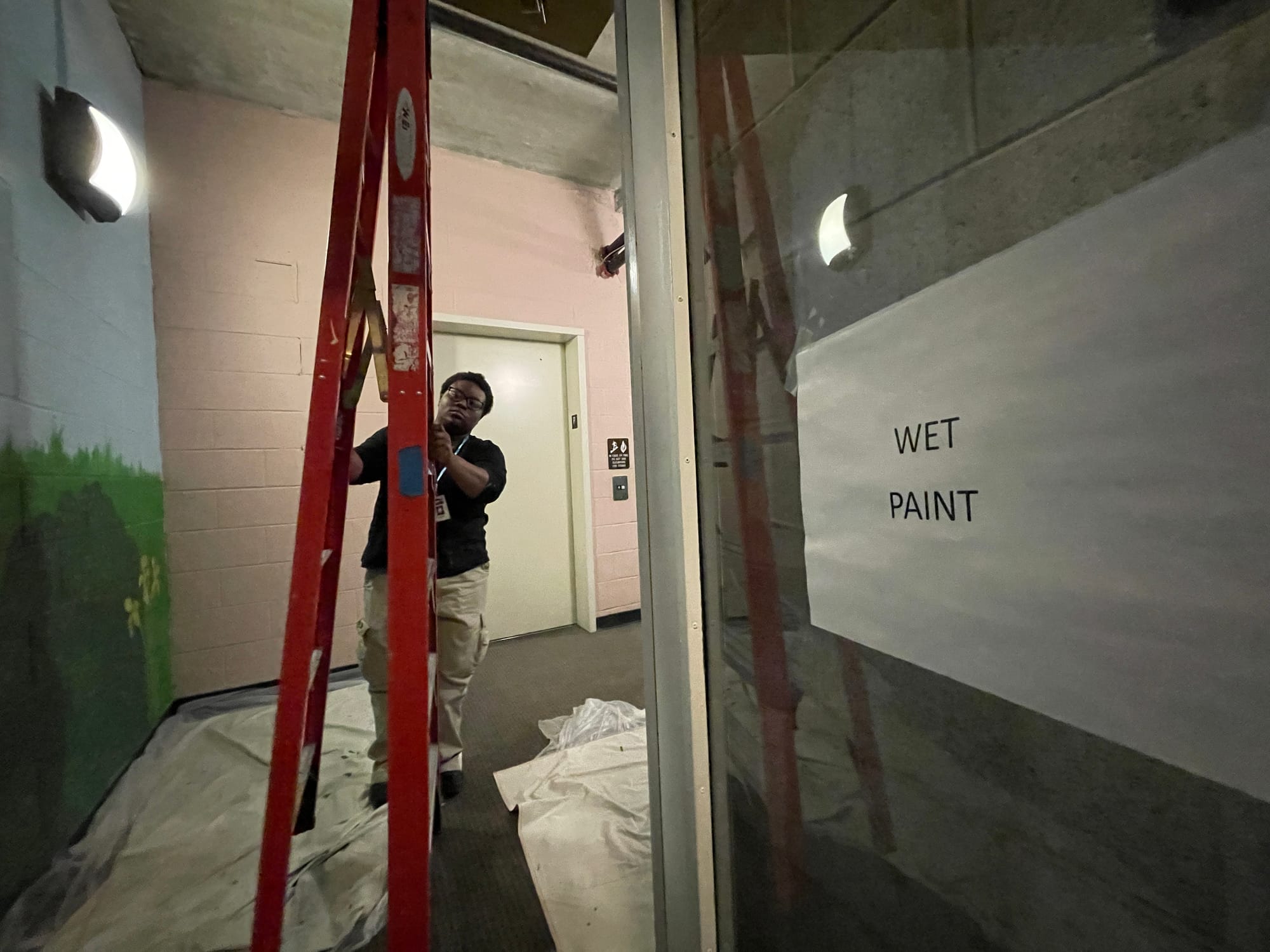 Nalah Brown sets up a ladder to work at the clouds on the upper part of the center wall.