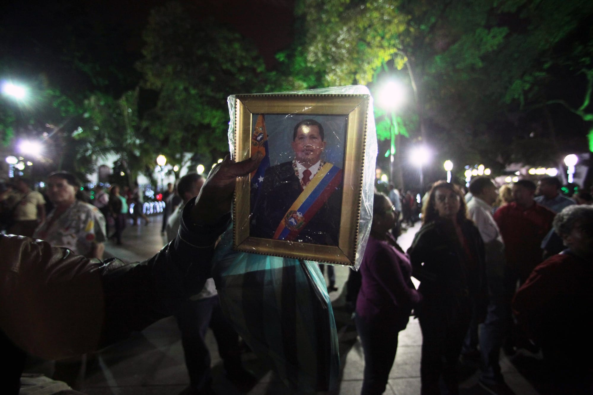 A man holds up an image of Chavez as people gather to pray for him at Simon Bolivar Square in Caracas on Dec. 11, 2012. Chave