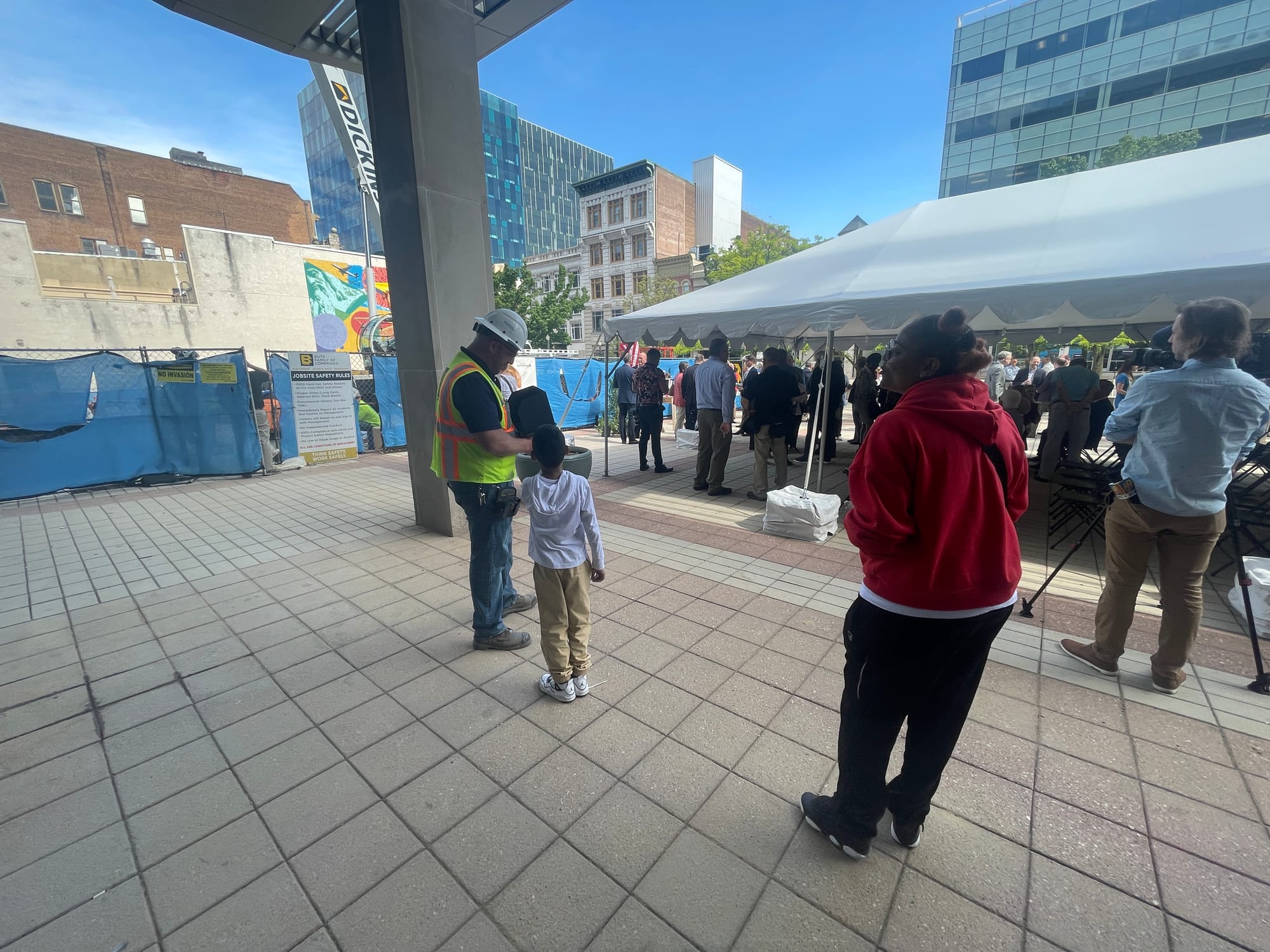 A member of the construction team uses a controller to fly a drone, capturing video of the day. The boy came up and wanted to