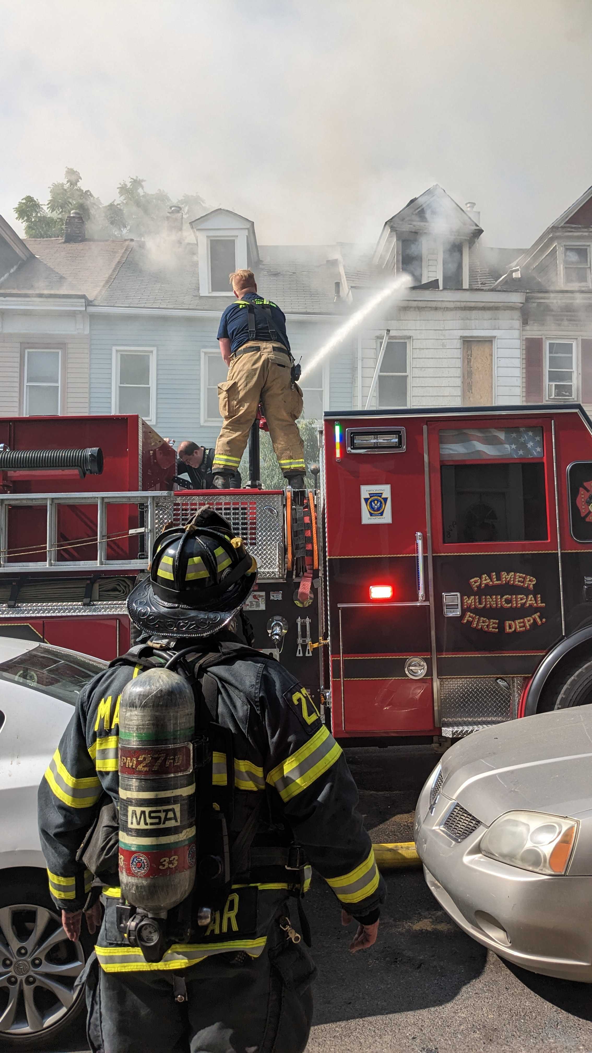 A man stands on a fire truck, as he tries to fight the fire.