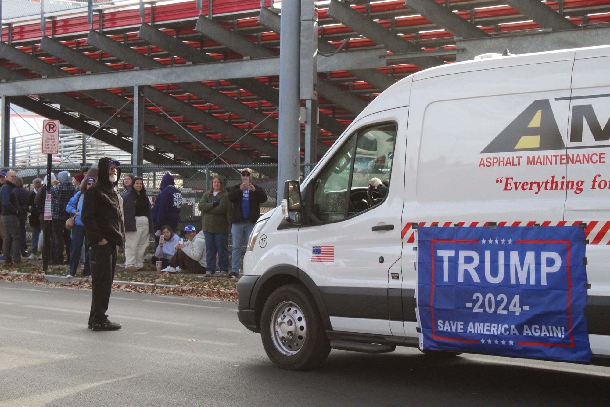 An asphalt maintenance solutions van with Donald Trump flags attached drove past hundreds of Kamala Harris rally attendees li