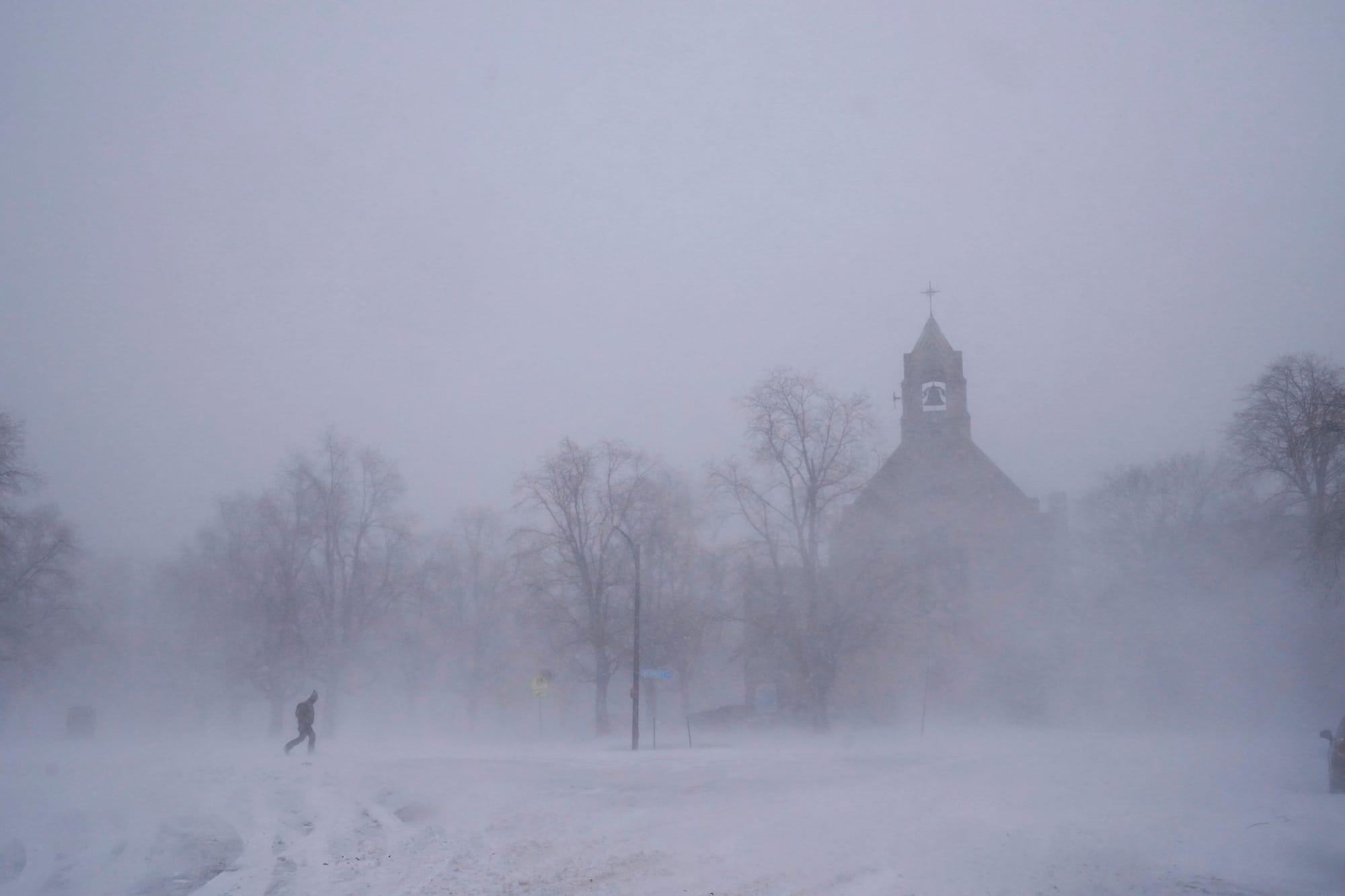 A lone pedestrian in snow shoes makes his way across Colonial Circle as St. John's Grace Episcopal Church rises above the blo