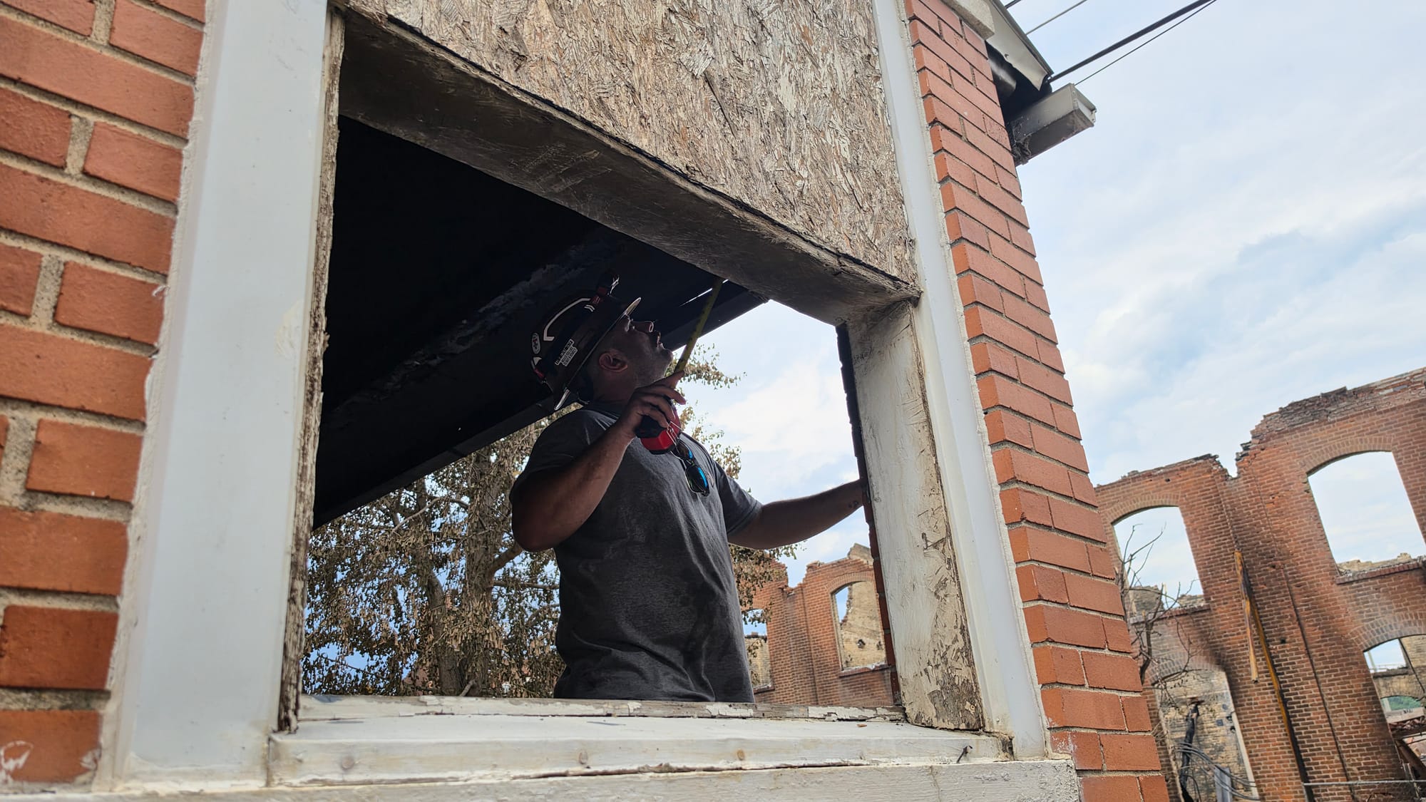 A worker measures a piece of a porch at one of the seven rowhomes damaged by the blaze at the former American Atelier factory