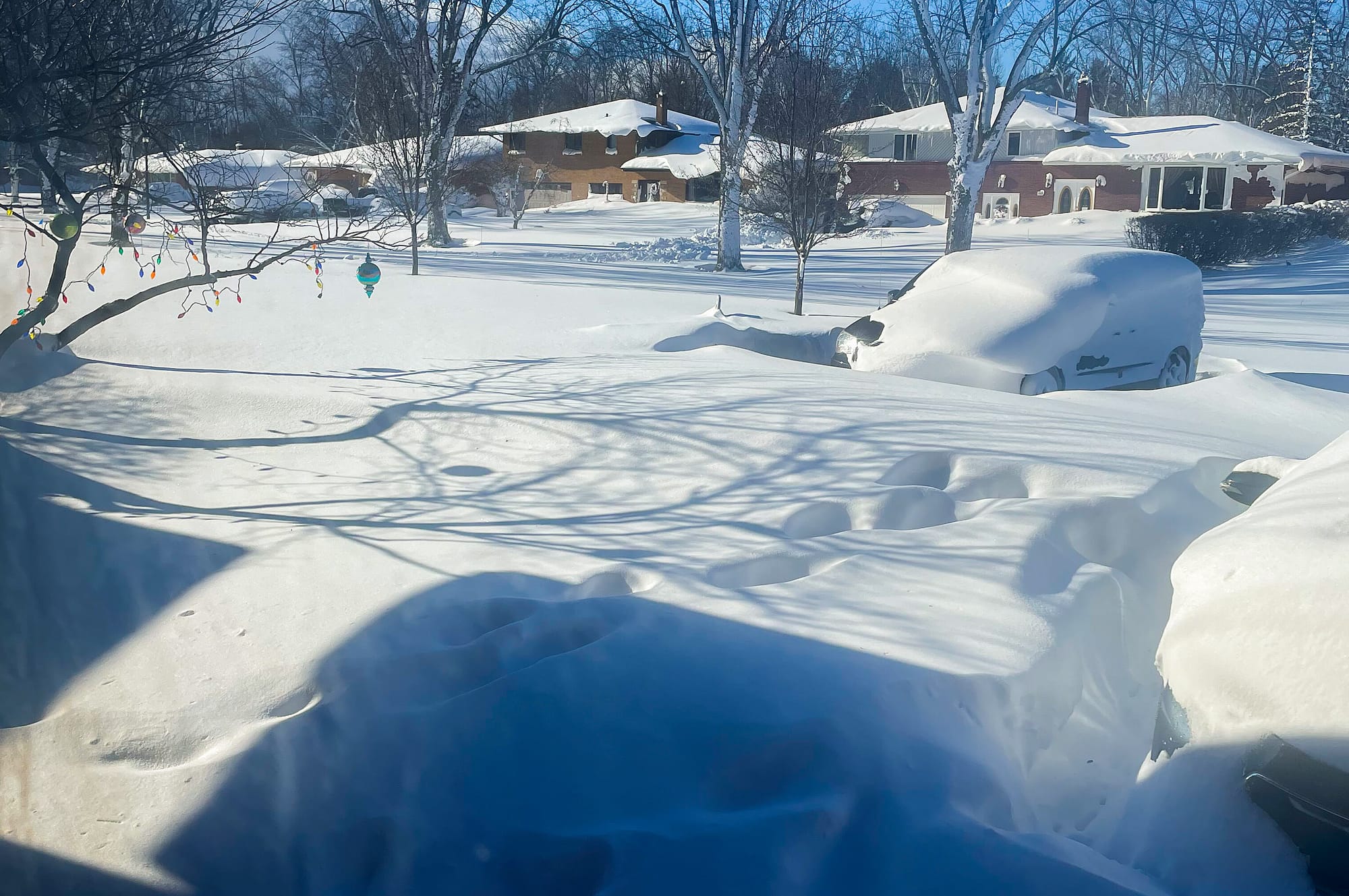 A car sits blanketed in snow on a driveway, Sunday, Dec. 25, 2022, in Amherst, N.Y. Millions of people hunkered down against 