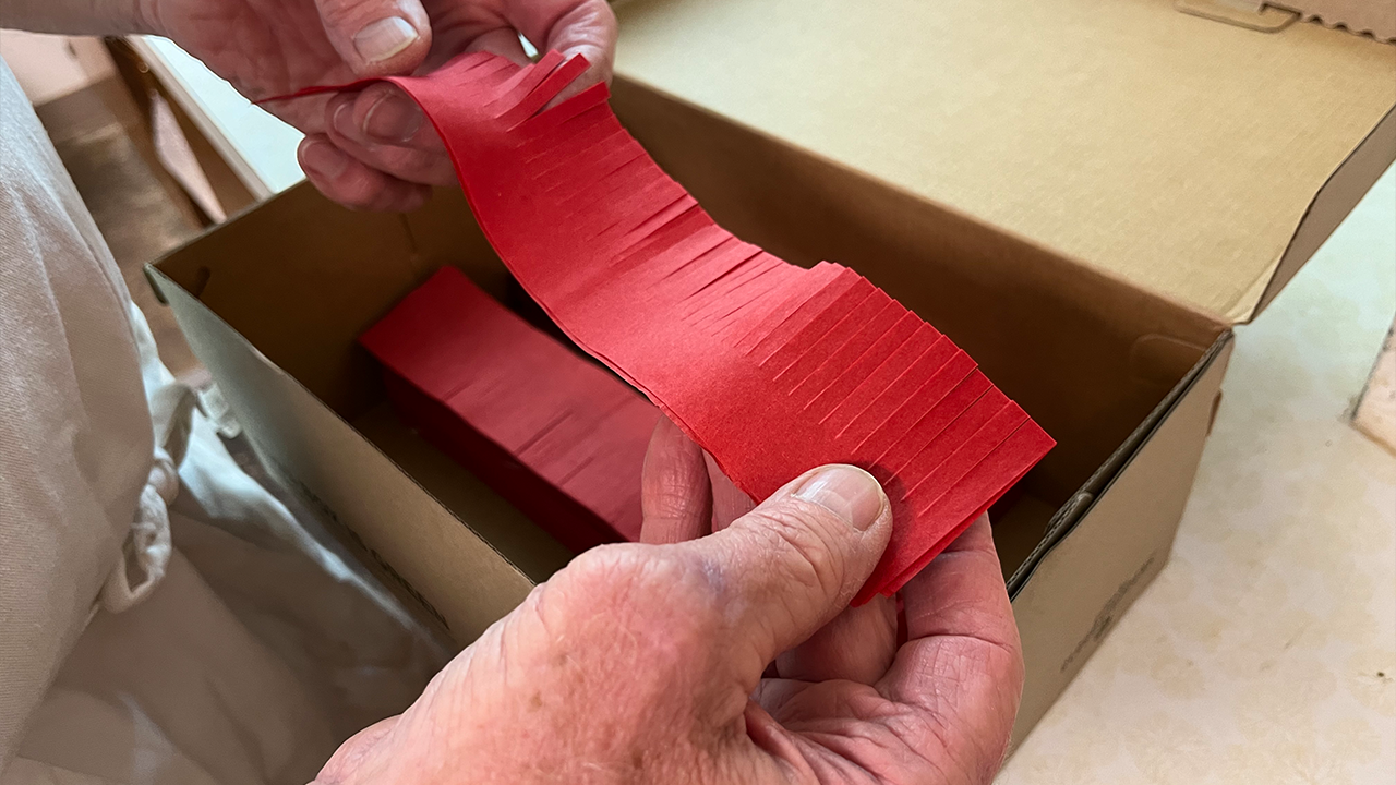 The folded tissue paper layers are fringed by machine before volunteers glue them to the 6-inch candles.