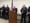 A man in a suit speaks at a podium, flanked by police officers in uniform.